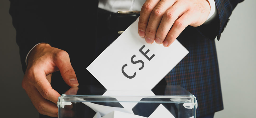 vote-cse Mains glissant un bulletin portant l'inscription CSE dans une urne transparente, illustrant le processus d'élections du Comité Social et Économique